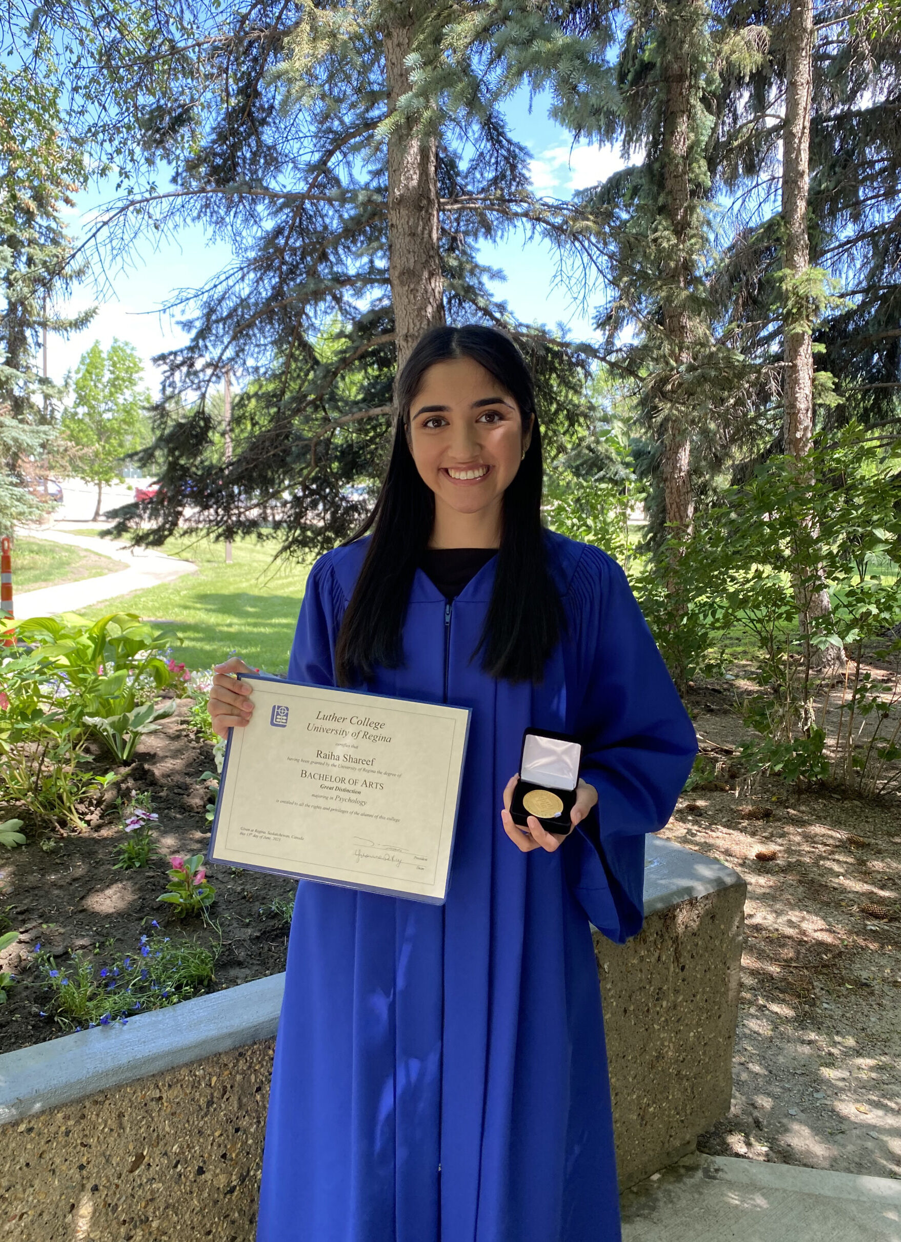 Image of Raiha Shareef outside with her diploma and medal of distinction